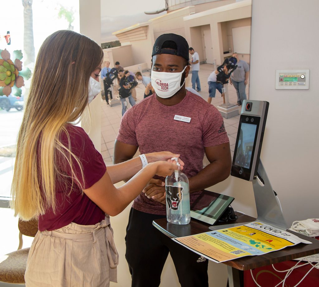 Students wearing face masks undergo campus COVID-19 screening with temperature checks and hand sanitizer