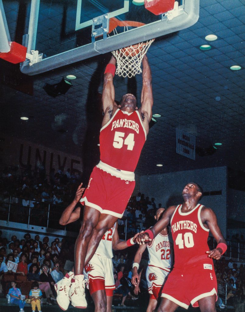 Man dunking a basketball in front of a crowd and among three other players