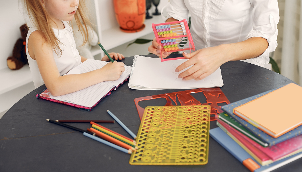 Female child writing with a pencil next to an adult holding an abacus