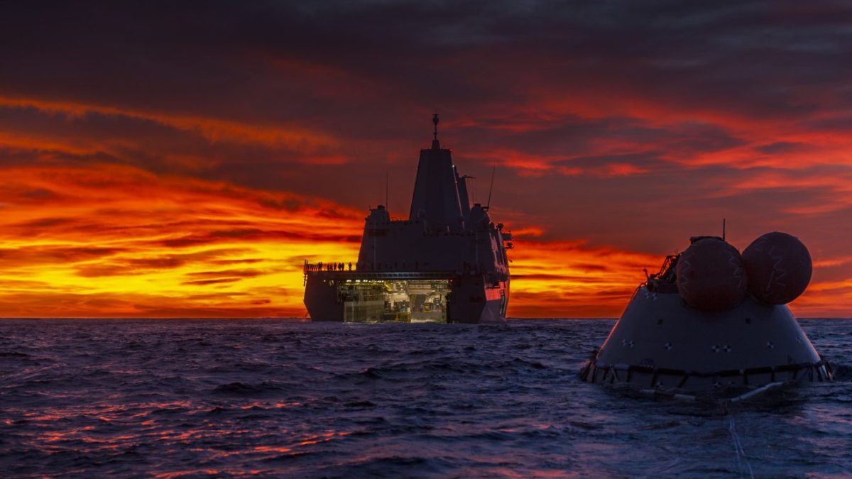 Recovery ship and space capsule in ocean in background with space capsule in foreground.
