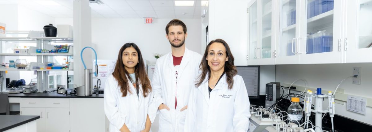 Professor stands with two students in a laboratory looking at the camera.