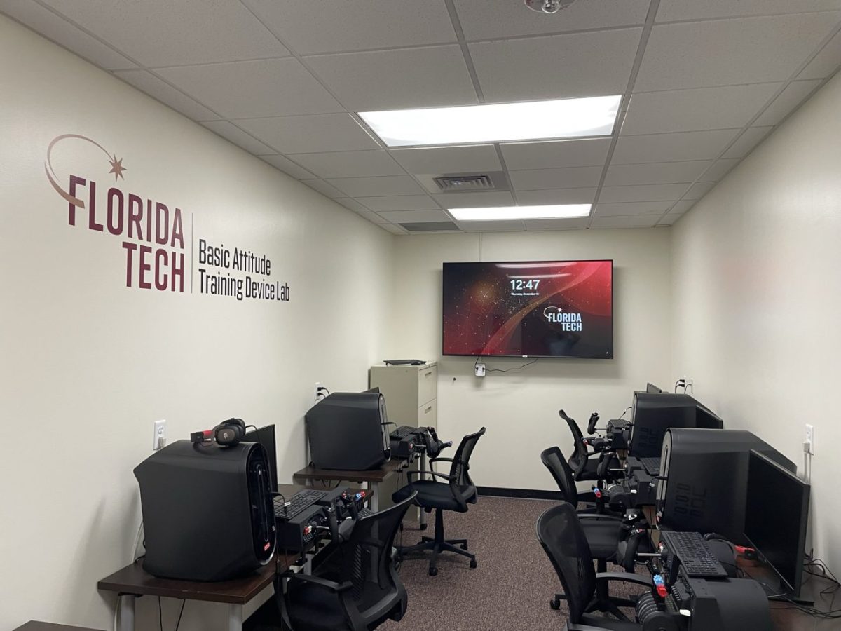 A room with computers, tables, chairs and a screen on the wall.