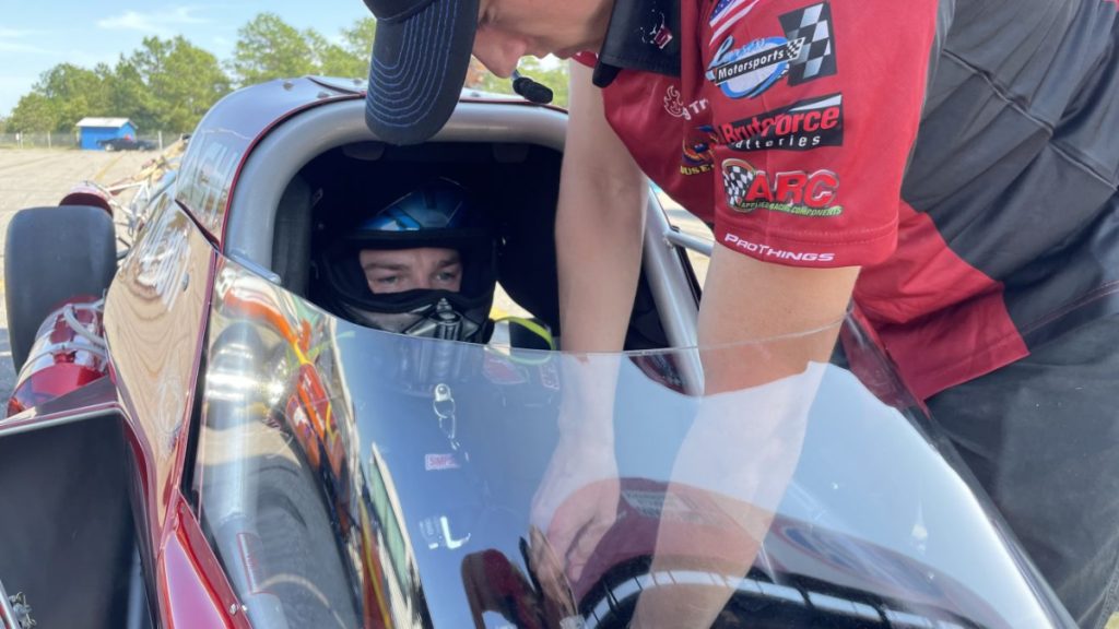 driver in the cockpit of a drag racer, getting strapped in